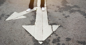 A person standing on arrows painted on pavement. One arrow points forward and one points to the left.