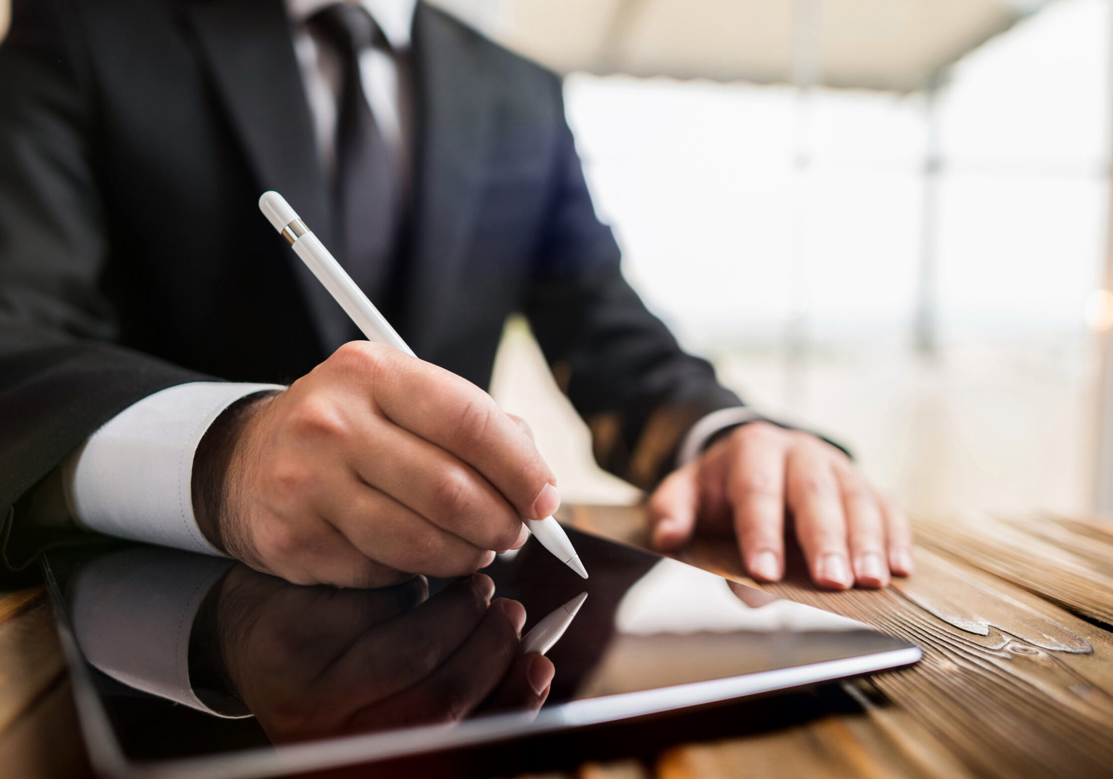 Man in a suit writing on a tablet with a stylus