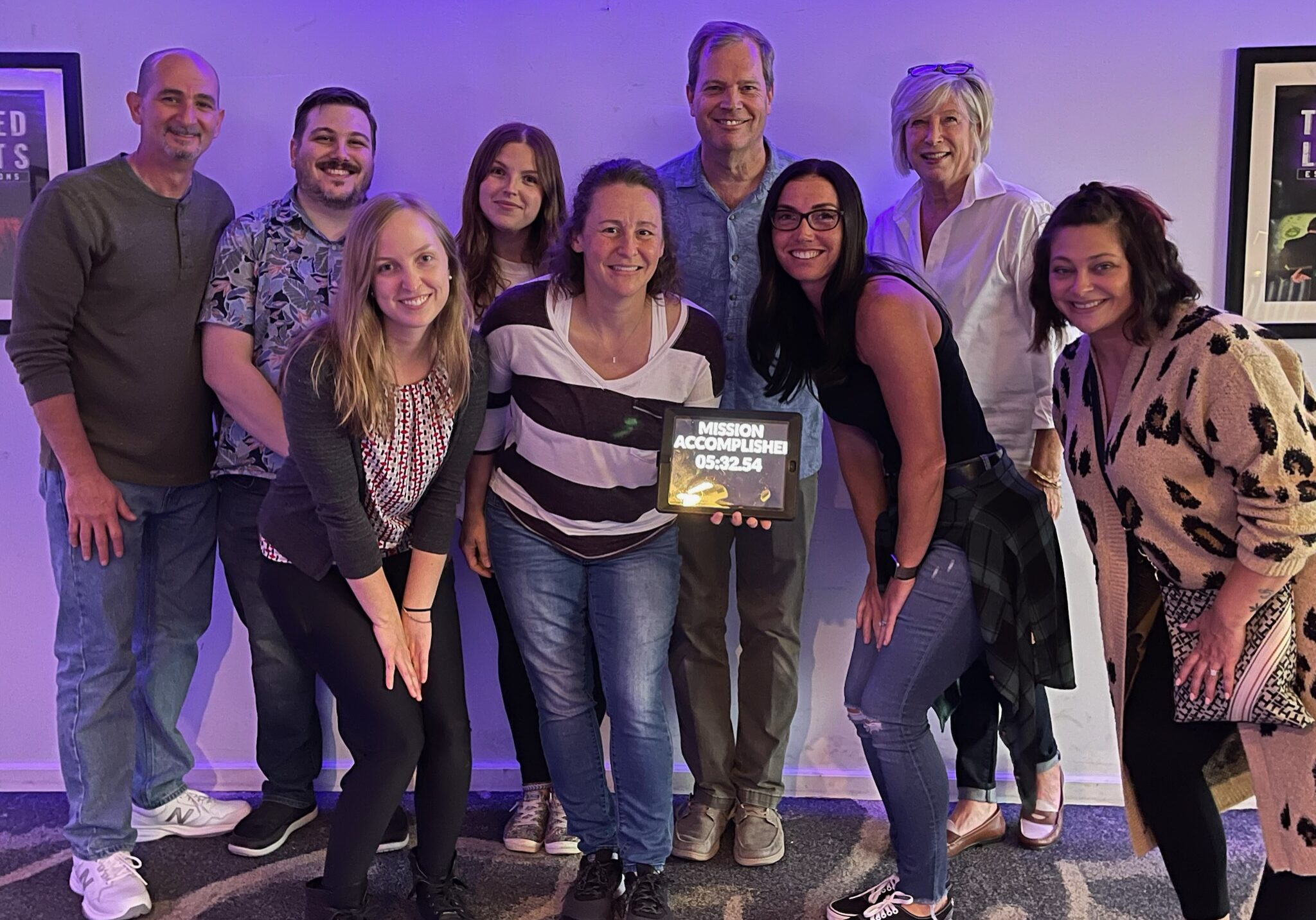 A group of men and women posing for a photo holding a mission accomplished sign